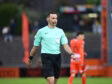 Soccer referee in a mint green shirt with a headset, walking on the pitch during a match.
