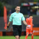 Soccer referee in a mint green shirt with a headset, walking on the pitch during a match.
