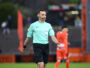 Soccer referee in a mint green shirt with a headset, walking on the pitch during a match.
