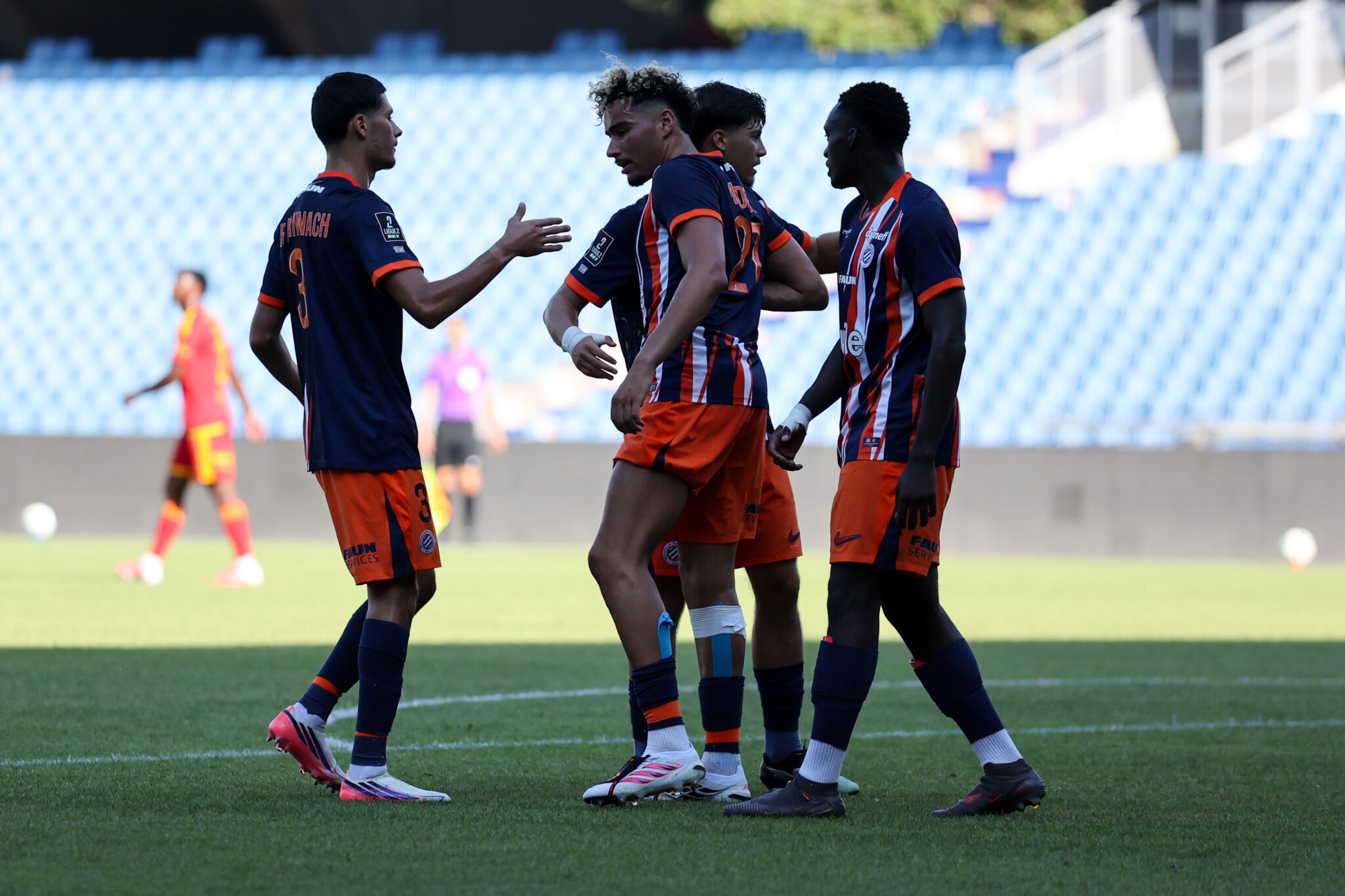 Four soccer players in blue and orange uniforms celebrate or greet each other on the field.