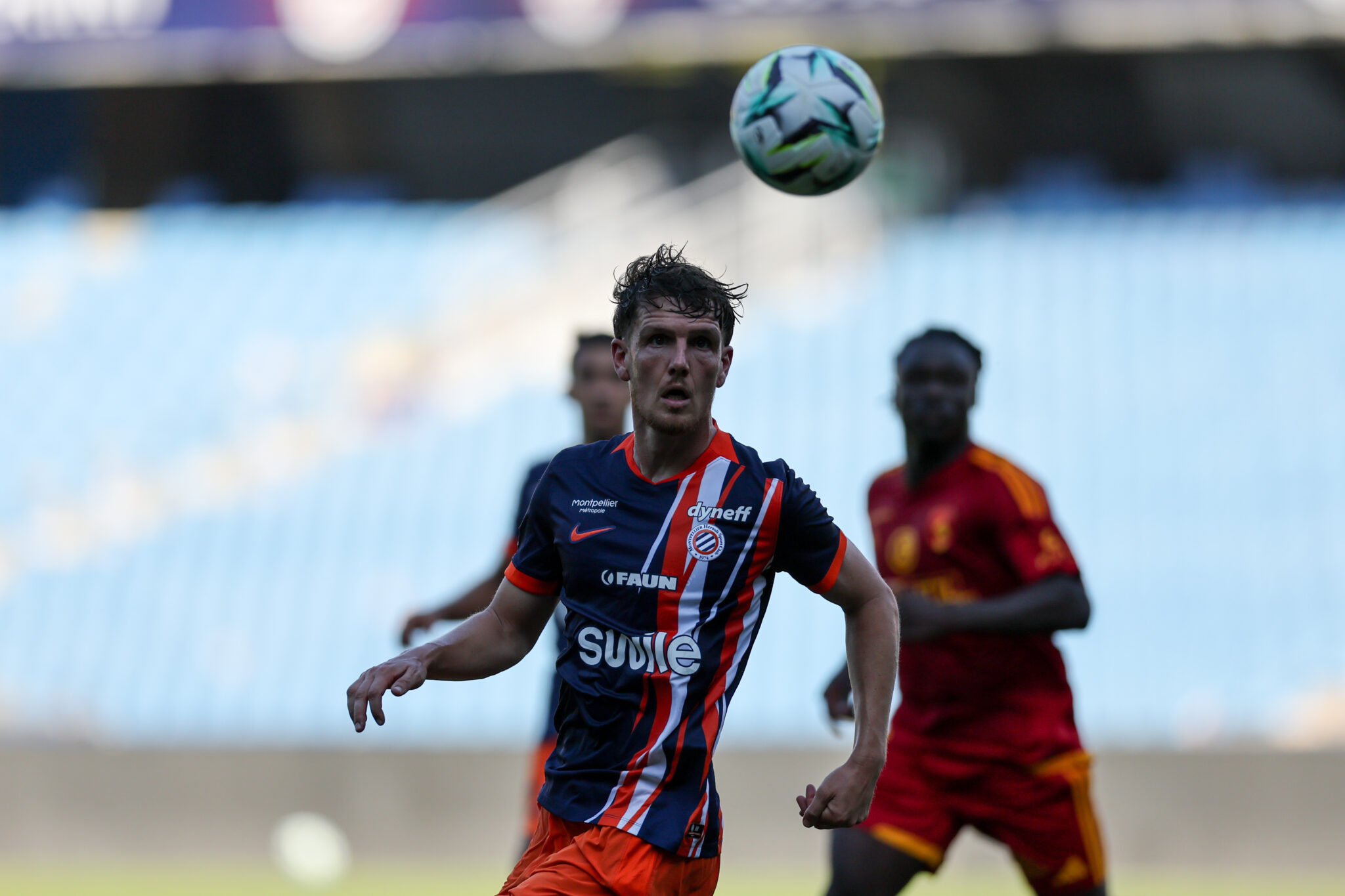 Julien Laporte Montpellier Herault SC v Rodez Aveyron Football - Friendly Match 01082026 | AllezPaillade.com Soccer player in a blue-red striped kit looks up at a ball suspended above his head during a match, with teammates in the background.