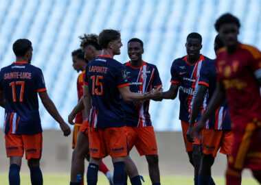Group of young soccer players in blue and orange jerseys greet each other with handshakes and smiles on a grassy field.