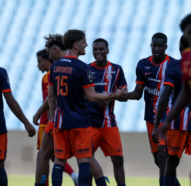 Group of young soccer players in blue and orange jerseys greet each other with handshakes and smiles on a grassy field.
