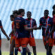 Group of young soccer players in blue and orange jerseys greet each other with handshakes and smiles on a grassy field.