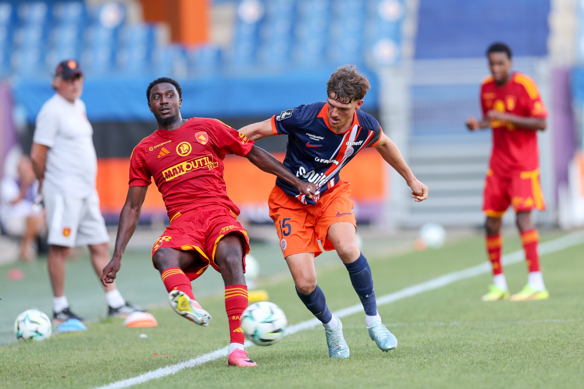 Julien Laporte Montpellier Herault SC v Rodez Aveyron Football - Friendly Match 01082026 | AllezPaillade.com Two soccer players contest possession on the field, one in a red kit and the other in blue and orange, chasing a ball amid other players in the background.