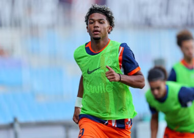 Soccer player in a bright green training bib runs on a field with blurred teammates in the background.