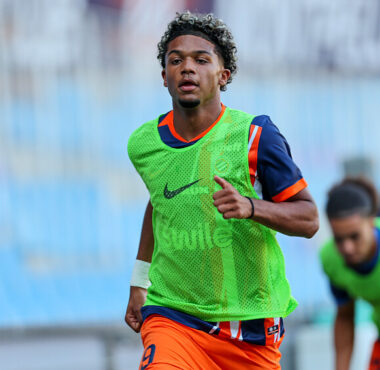 Soccer player in a bright green training bib runs on a field with blurred teammates in the background.