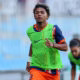 Soccer player in a bright green training bib runs on a field with blurred teammates in the background.