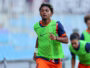 Soccer player in a bright green training bib runs on a field with blurred teammates in the background.