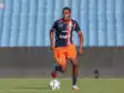 Soccer player in navy and orange kit dribbling a ball on a green field with stadium seats in the background