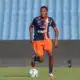 Soccer player in navy and orange kit dribbling a ball on a green field with stadium seats in the background