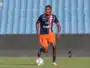 Soccer player in navy and orange kit dribbling a ball on a green field with stadium seats in the background
