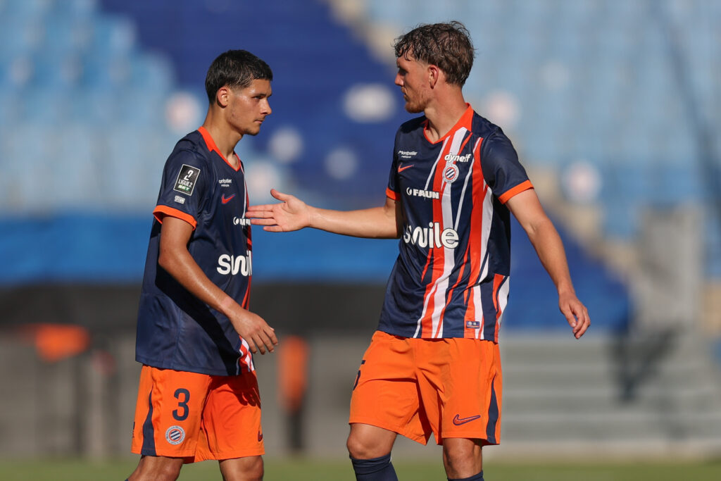 Laporte Naoufel El Hannach Montpellier Herault SC v Rodez Aveyron Football - Friendly Match 01082026 | AllezPaillade.com Two soccer players in navy and orange kits greet each other with a handshake on the field during a match.