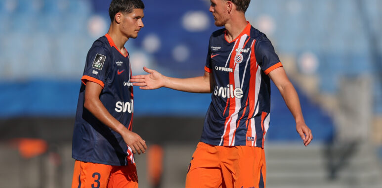 Laporte Naoufel El Hannach Montpellier Herault SC v Rodez Aveyron Football - Friendly Match 01082026 | AllezPaillade.com Two soccer players in navy and orange kits greet each other with a handshake on the field during a match.