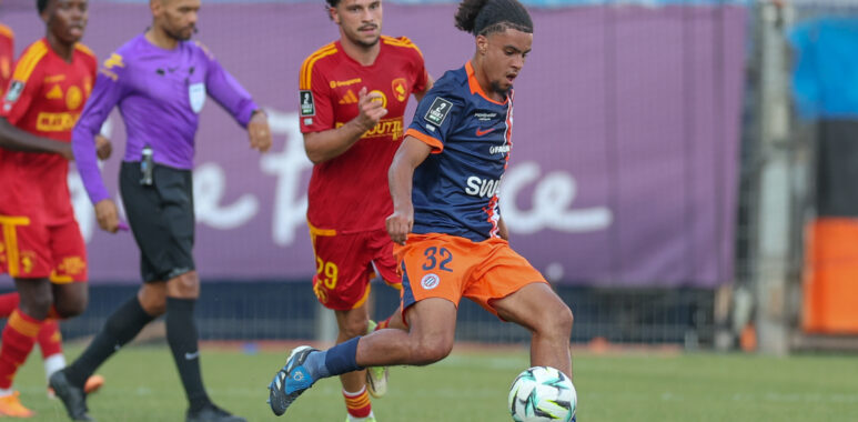 Montpellier Herault SC v Rodez Aveyron Football - Friendly Match 01082026 | AllezPaillade.com Soccer match action with a blue-jersey player dribbling the ball as red-jersey opponents chase behind on a green field.