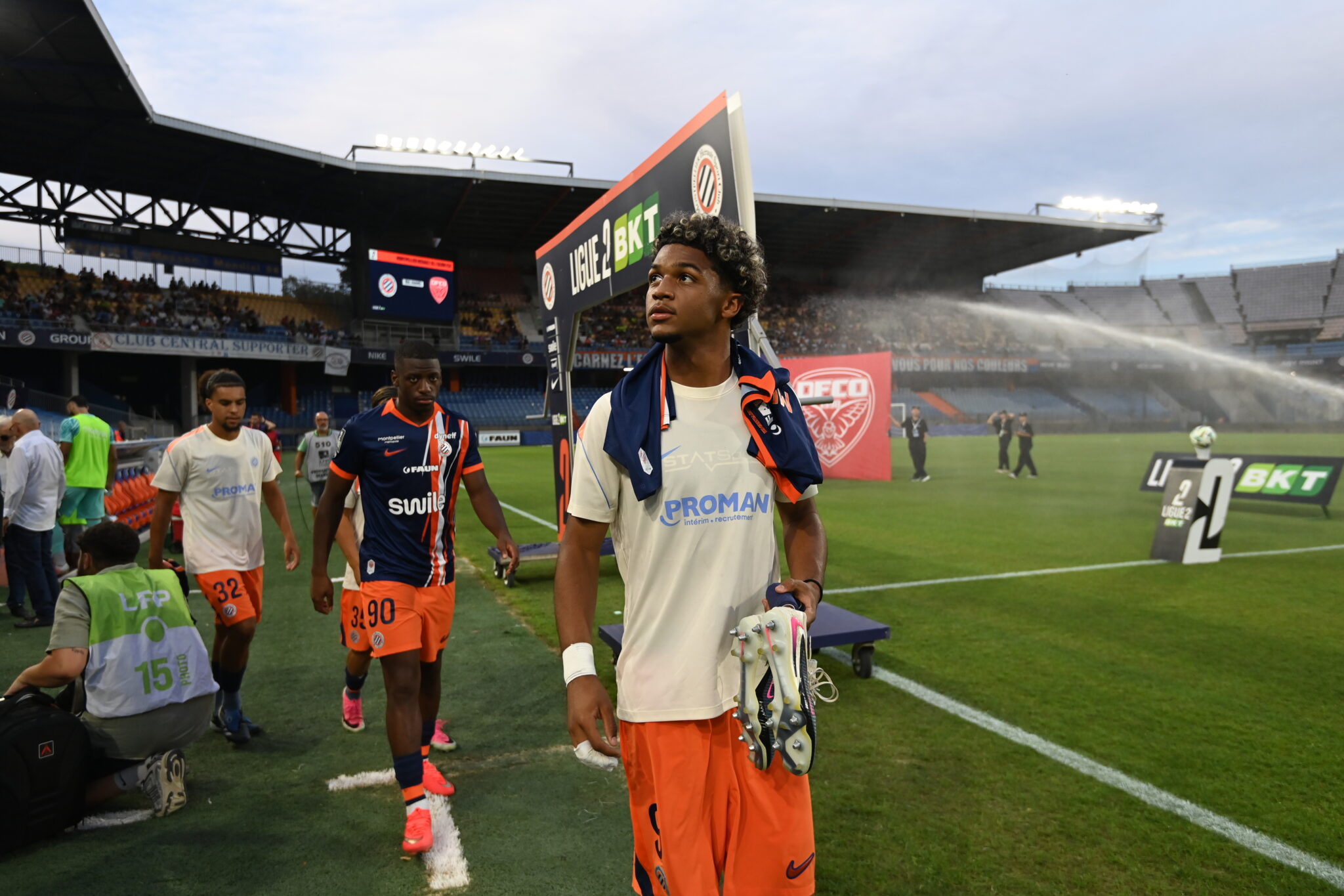 Mégnan | AllezPaillade.com Soccer players walk off the field near the sideline with a stadium crowd in the background.