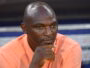 Close-up of a man in a peach shirt resting his chin on his hand, looking pensive.