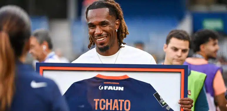 Montpellier Herault SC v Dijon FCO - Ligue 2 BKT 20262027 | AllezPaillade.com Smiling man with dreadlocks holding a framed jersey displaying the number 100 at an event.