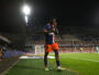 Soccer player in a blue and orange jersey number 19 standing near the sideline during a night match, stadium filled with spectators in the background.