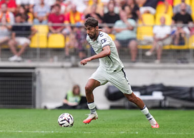 Yanis Zouaoui Le Mans FC v Le Havre Athletic Club - Friendly Match - 15082026 | AllezPaillade.com Soccer player in a white kit dribbling the ball on a green pitch with a blurred crowd in yellow seats behind him.