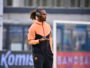 Athlete wearing a peach and black tracksuit with over-ear headphones, holding a phone on a sports field surface.