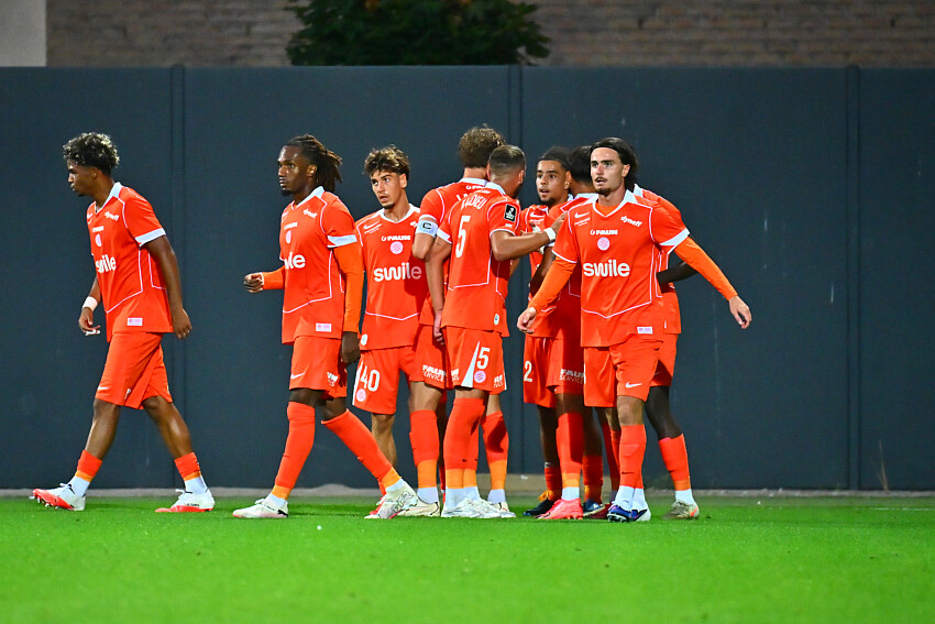 Joie | AllezPaillade.com Group of soccer players in bright orange uniforms standing together on a green pitch, celebrating.