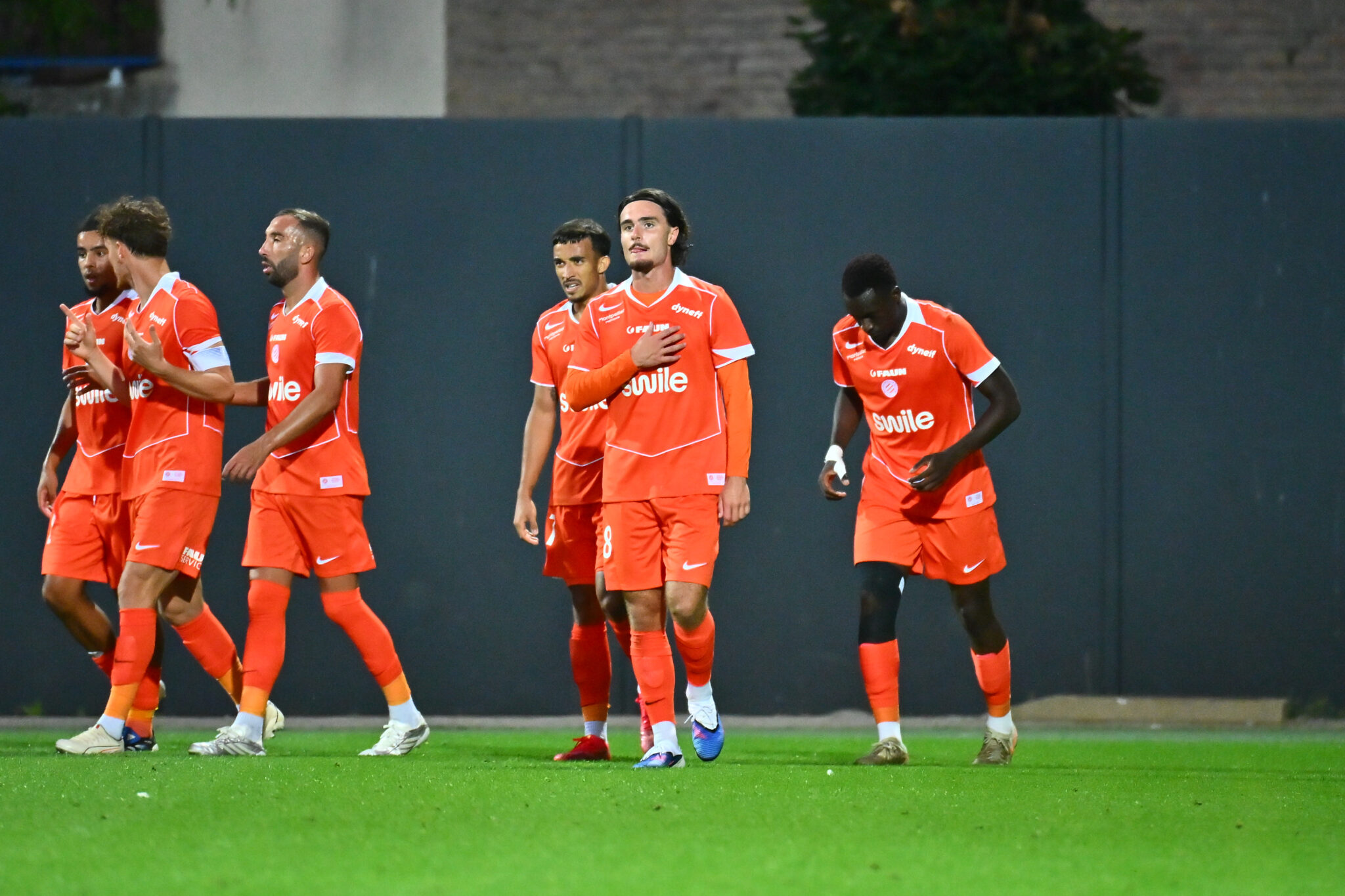 Group of soccer players in orange jerseys walking across a green field after a match.