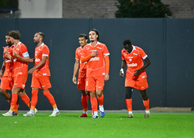 Group of soccer players in orange jerseys walking across a green field after a match.
