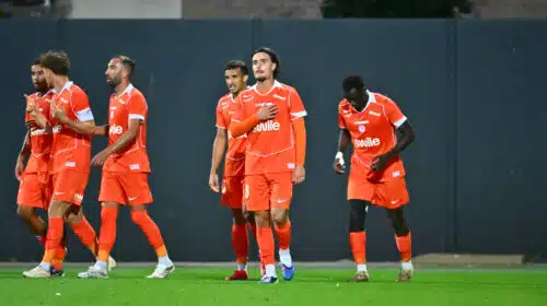 Group of soccer players in orange jerseys walking across a green field after a match.