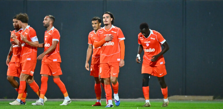 USL Dunkerque v Montpellier HSC - Ligue 2 BKT 20262027 | AllezPaillade.com Group of soccer players in orange jerseys walking across a green field after a match.