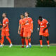 Group of soccer players in orange jerseys walking across a green field after a match.