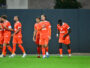 Group of soccer players in orange jerseys walking across a green field after a match.