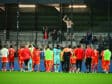 Soccer players in red celebrate on the field as fans cheer from the stands after a match.