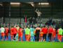 Soccer players in red celebrate on the field as fans cheer from the stands after a match.