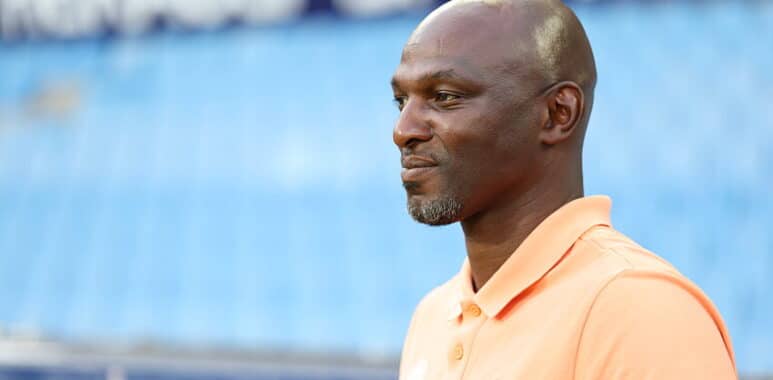 Profile view of a man in a peach polo shirt standing at a sports stadium, looking to the right.