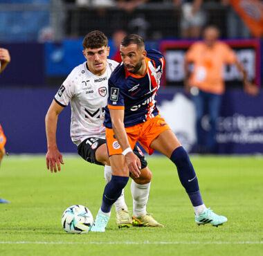 Soccer players in blue-orange and white chase the ball during a match on a sunny field.