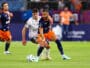 Soccer players in blue-orange and white chase the ball during a match on a sunny field.