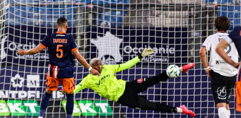 Soccer scene: goalkeeper in neon green dives to stop a shot as players watch near the goal net.