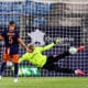 Soccer scene: goalkeeper in neon green dives to stop a shot as players watch near the goal net.