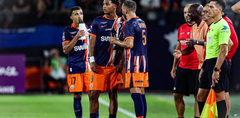 Soccer players in blue-orange uniforms standing on the field with coaches and officials nearby during a match.
