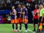 Soccer players in blue-orange uniforms standing on the field with coaches and officials nearby during a match.