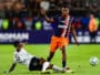 Soccer match moment: a blue-and-orange team player stands over a sliding white-jersey defender as the ball rolls nearby.