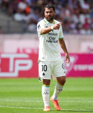 Soccer player in a white kit with number 10, pointing during a match on a green field.