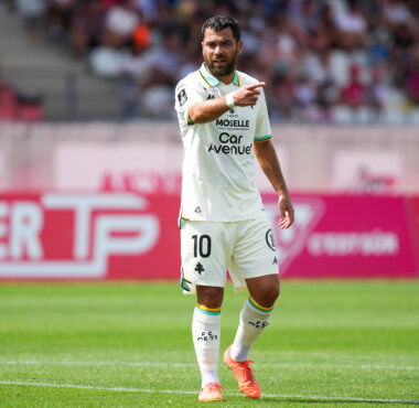 Soccer player in a white kit with number 10, pointing during a match on a green field.