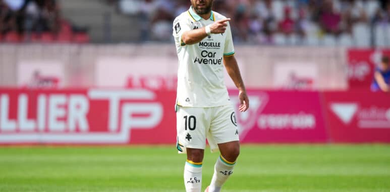 Soccer player in a white kit with number 10, pointing during a match on a green field.