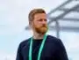 Man with a reddish beard wearing a black shirt and a green lanyard, standing outdoors and looking to the right.