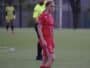 Female soccer player in a red uniform with number 9 stands on a green field; a referee in a neon yellow shirt is behind her.