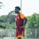 Male soccer player in maroon and orange kit stands with hands on hips on a grassy field during training.