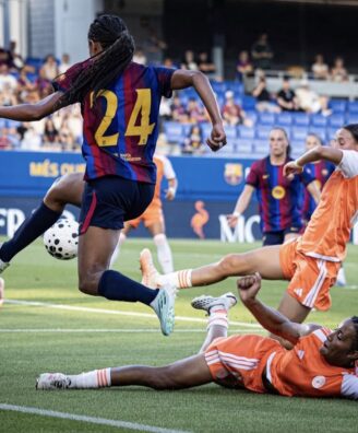 Screenshot | AllezPaillade.com Soccer match scene: a player in a maroon-and-blue jersey (#24) leaps to kick the ball while players in orange defend nearby on a green field.