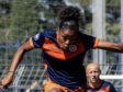 Screenshot | AllezPaillade.com Female soccer player in a navy and orange uniform mid‑stride, arms outstretched, on a grassy field during a match with a teammate in the background.